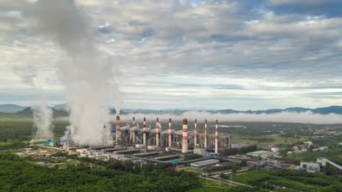 Aerial view over coal-fired power plant at sun dawn with smoke from cooling,