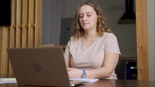 Woman Works at Laptop with Notebook at Home