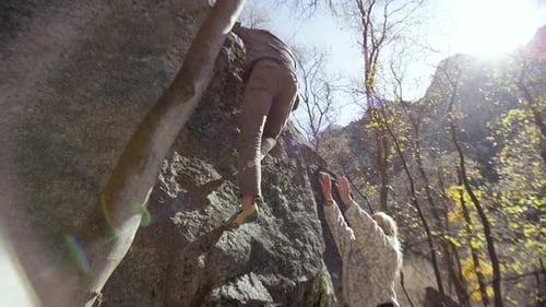 Man Climbing Rock with Woman Spotting in Nature