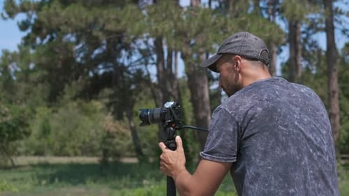 Man Adjusting Camera on Tripod in a Park