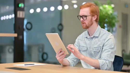 Red-Haired Man Using Tablet in Office Reacts Badly