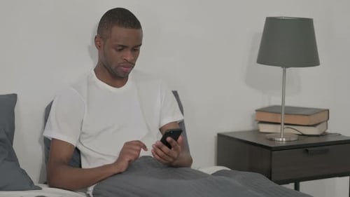 Man Looking Anxious at Phone in Bed