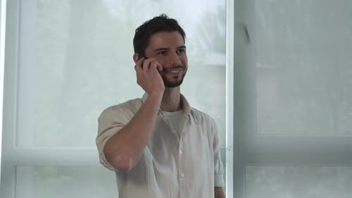 Young Man Talking on Phone Indoors by Blinds
