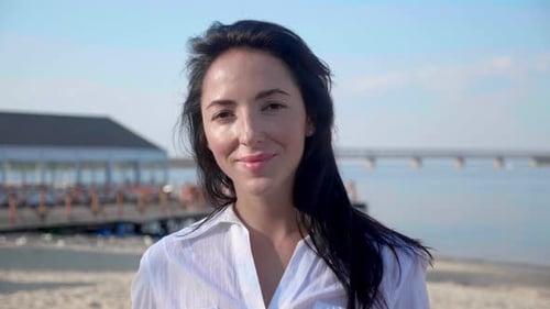 Portrait of Young Brunette Woman Looking at Camera Standing on the Beach with a Sea on Background