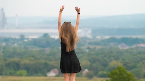 Back View of a Young Energetic Woman with Long Hair in Short Summer Dress Dancing Happily in Nature