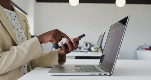 Close up of hands of african american businesswoman sitting at desk using smartphone
