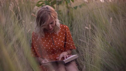 Beautiful Happy Young Woman in Field of Spikelets and Wheat with Book on the Sunset Blonde in the
