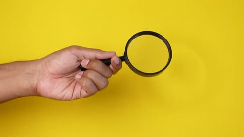 Handhaltende Lupe vor gelbem Hintergrund