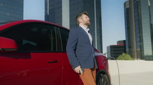 Intelligenter Geschäftsmann mit Smartphone, das auf den Akku eines Elektrofahrzeugs wartet