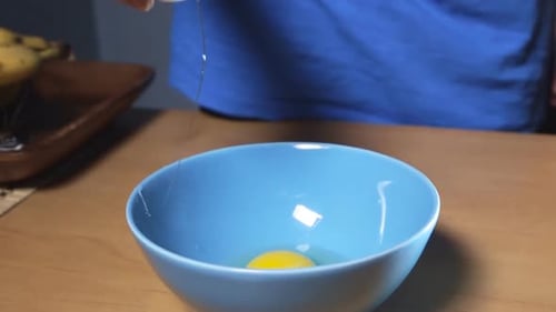 Cracking Eggs into a Blue Bowl on Table