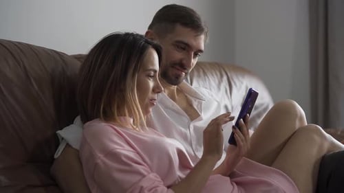 Couple Using Smartphone Relaxing Together on Couch Indoors