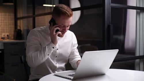 Man Working on Laptop and Talking on Phone