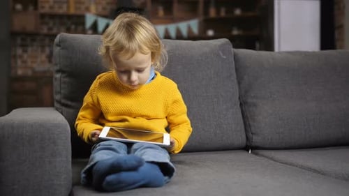 Joli petit garçon blond utilisant le pavé tactile sur le canapé