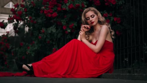 Fabuleuse fille aux lèvres rouges dans une robe rouge sur un superbe fond de roses d'été. Portrait de femme fantastique