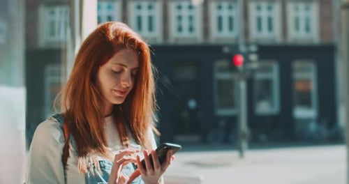 Young woman smiling and using a smartphone in the street