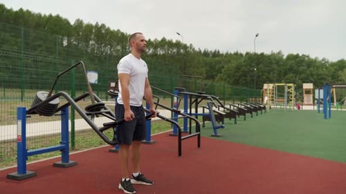 Young Man Does a Deadlift Exercise on a Simulator at the Stadium