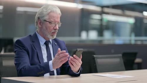 Senior Businessman Uses Mobile Phone at Conference Table