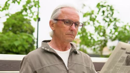 Senior Man in Glasses Reading Newspaper in the Park