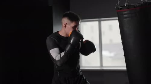Fit and Concentrated Young Man Boxer Hitting the Punching Bag in the Gym