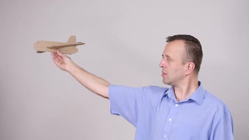 Man Holding Cardboard Airplane Against Gray Background