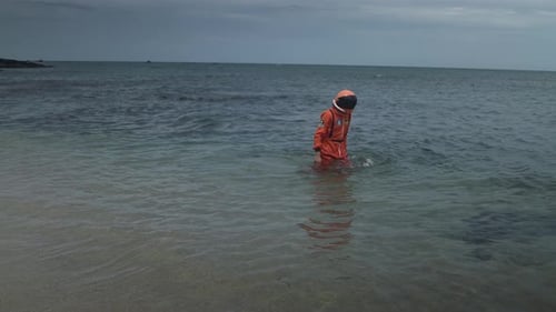 Lone Astronaut Stands in Ocean on Overcast Day
