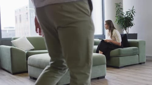 Dos compañeras de trabajo diversas sentadas en el sofá con documentos y una tableta hablando