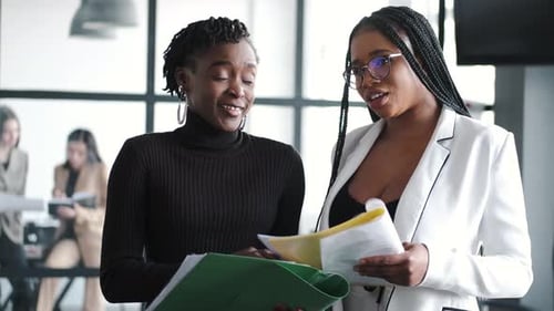 Two Women Discuss Business Documents in Modern Office