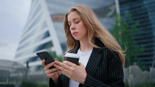 Young Woman Uses Phone with Coffee in City