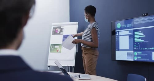 Diverse business people wearing face masks sitting listening to presentation in office