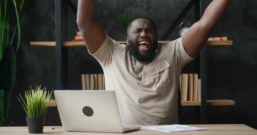 Happy African Businessman Dancing Cheerfully While Working at Laptop Computer in Home Office