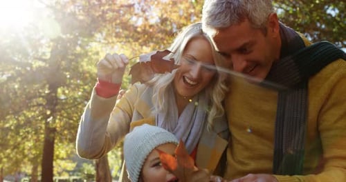 mamá, papá e hija sosteniendo hojas y sonriendo al aire libre