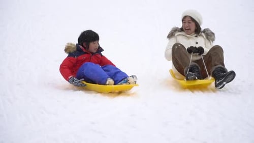 Asiatische Mutter und ihr Sohn spielen Schlitten im Schneefall