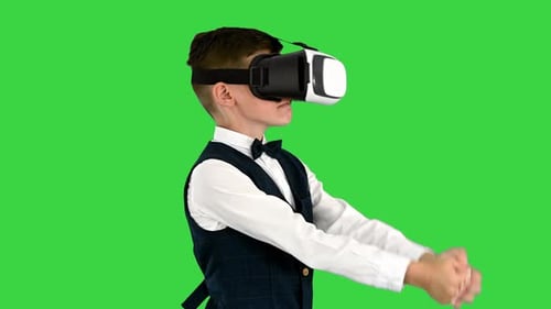 Excited Boy in Formal Wear Playing the Sword Game in Virtual Reality Goggles on a Green Screen