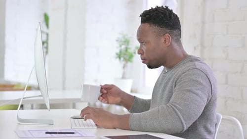 Enttäuschter gelegentlicher afrikanischer Mann arbeitet im Büro am Desktop