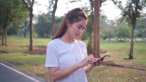 Woman Using Phone and Listening to Music in Park
