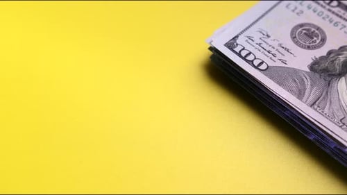 Stack of One Hundred Dollar Bills on Yellow Background