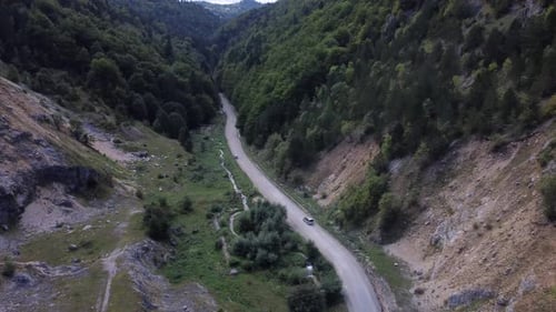 A Wide Drone Shot Tracking a Car Driving a Road Moving Through the Wilderness