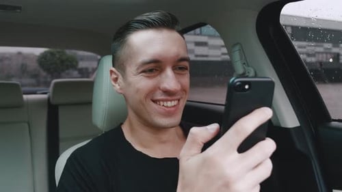 Smiling Man Using Smartphone in Car