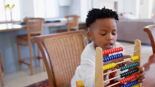 Vista frontal de un niño negro jugando con un ábaco en una cómoda casa 4k