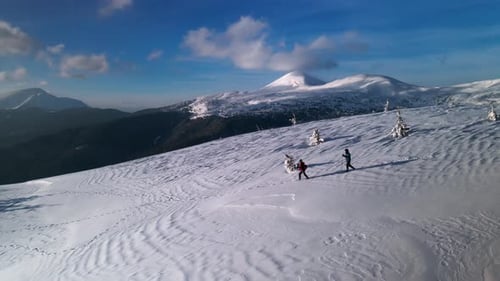 Drone Flying Over Young Couple of Hikers, Descending a Mountain Ridge in Winter