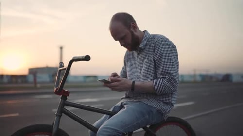 Young Man with Bmx Bicycle Uses His Phone at Sunset on the Street
