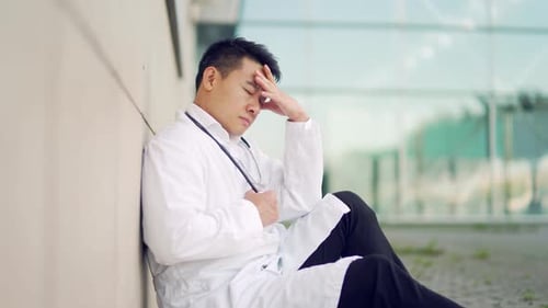 portrait stressful Asian doctor sitting or standing outside a hospital