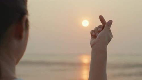 Dedo de silueta en forma de mini corazón en una playa marina al atardecer tropical
