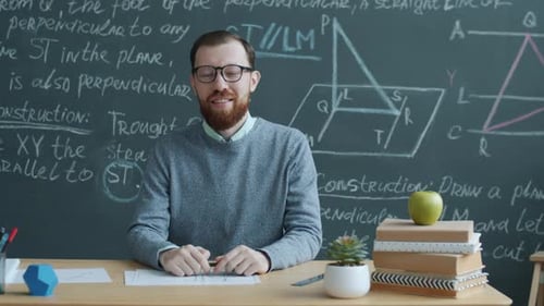 Portrait of University Professor Sitting at Desk in Class with Chalkboard in Background