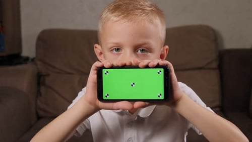 Porträt eines Jungen zu Hause Er hält ein Smartphone mit einem Greenscreen