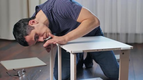 Young Man Assembling Small White Table Indoors