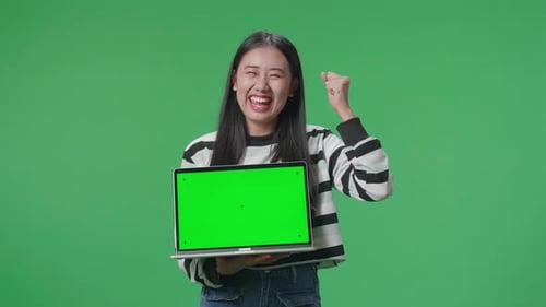 A Happy Asian Woman Celebrating While Holding Green Screen Computer In The Green Screen Studio