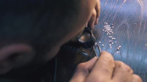 Person Inspecting Jewels with Magnifying Glass and Tweezers