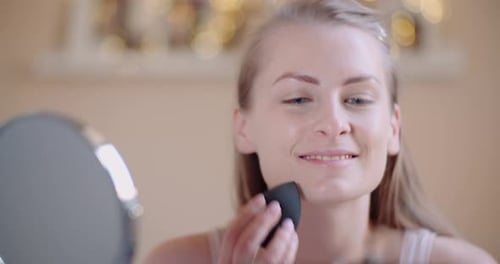Woman Applying Makeup with Black Sponge in Home