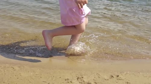 Close-up playful young caucasian girl in a pink skirt runs in the white sand of a beach
